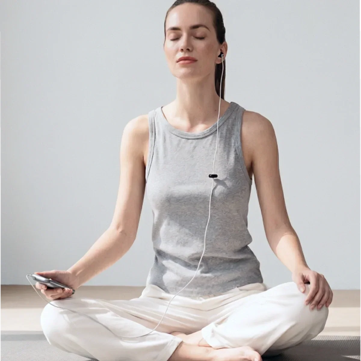 Woman sitting calmly while using a wired ear-based wellness device during a relaxation session